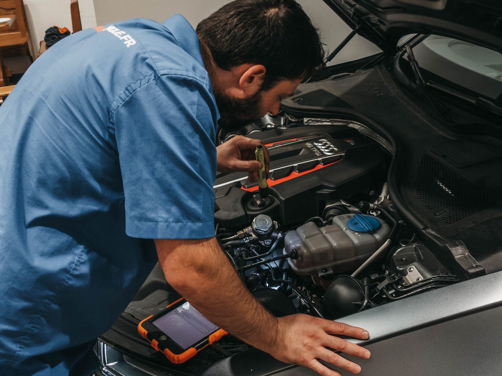 Mechanic checking an Audi engine bay with a torch and diagnostic tablet during a pre-purchase inspection